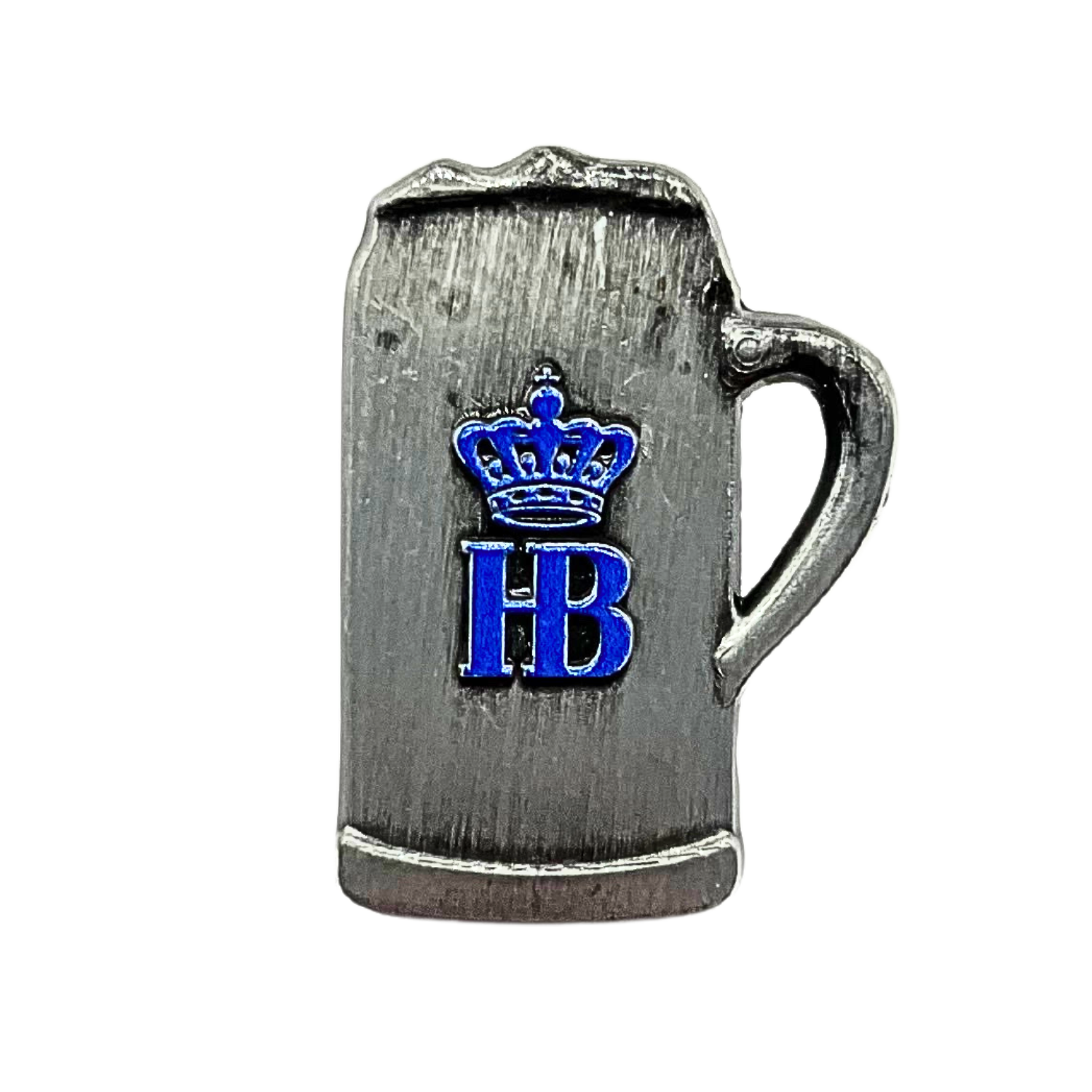 „Metallischer Pin in Form eines Bierkrugs mit Henkel auf der rechten Seite. Der Krug besteht aus gebürstetem Metall. Auf der Vorderseite befindet sich eine blaue Krone über den blauen Buchstaben ‚HB‘.“