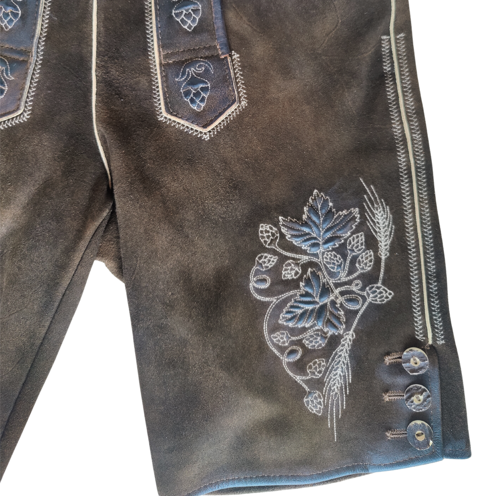 Detailansicht einer traditionellen braunen Lederhose mit heller Stickerei von Hopfen und Gerste sowie Zierknöpfen am Beinabschluss.
