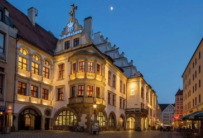 Beleuchtetes Hofbräuhaus München bei Abenddämmerung, historische Fassade mit Erker und Wappen unter klarem Nachthimmel.